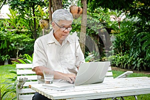 An elderly Asian man sitting at work typing a laptop at the front garden.