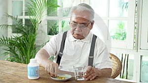 Elderly Asian man taking pill with cup of water at home