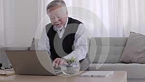 Elderly Asian man is working and note jobs on his laptop at home