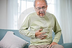 Elderly Asian old man sitting on sofa having stomachache