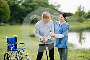 Elderly asian senior man on wheelchair with Asian careful caregiver and encourage patient, walking in garden. with care from a