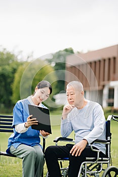 Elderly asian senior man on wheelchair with Asian careful caregiver. Nursing home hospital garden concept are walking in the