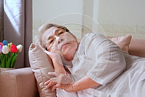 Elderly Asian woman with grey hair lying alone on the sofa. Aging society Sad and lonely concept, with copy space for text