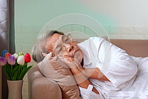 Elderly Asian woman with grey hair lying alone on the sofa. Aging society Sad and lonely concept, with copy space for text
