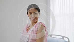 Elderly Asian woman in hospital showing plaster covering her arm after she has been vaccinated against COVID-19, health concept ,h