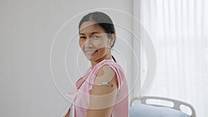 Elderly Asian woman in hospital showing plaster covering her arm after she has been vaccinated against COVID-19, health concept ,h