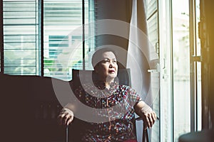 Elderly asian woman looking out the window at house,Senior having sorrowful and depressed
