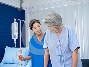 Elderly Asian woman patient trying to walk on walking frame held and carefully supported in arms.