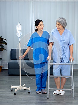 Elderly Asian woman patient trying to walk on walking frame held and carefully supported in arms.