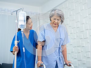 Elderly Asian woman patient trying to walk on walking frame held and carefully supported in arms.