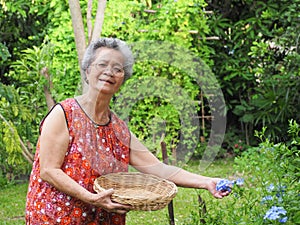 An elderly Asian woman smiling and holding a basket while standing in a garden. Concept of aged people and healthcare