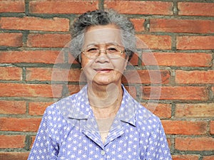 Elderly Asian woman smiling and looking at the camera while standing with a brick wall background. Concept of aged people and