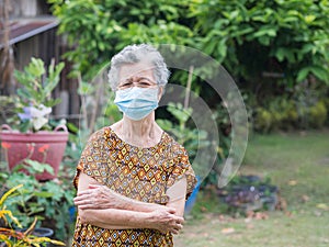 An elderly Asian woman wearing a face mask while standing in a garden