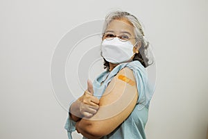 Elderly Asian woman wearing a mask in good health after vaccination against COVID-19 flu, showing thumbs up, UP looking at camera