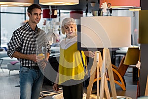 Elderly attractive lady choosing floor-lamp with young handsome man