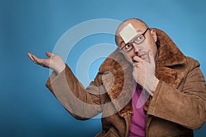 An elderly bald man in a fur coat has a blank post it on the forehead photo