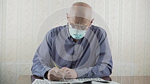Elderly bald person in protective face mask sloving crossword with pen