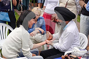 An elderly bearded Indian in a black turban gives a woman an acupressure of the hand