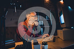 Elderly bearded programmer coding on a vintage computer while working at home office in the evening