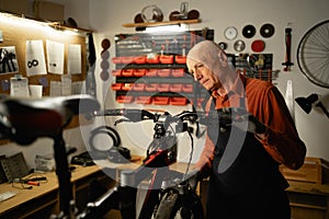 Elderly bicycle mechanic doing his professional work in workshop.