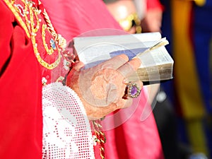 bishop with red cassock and the ancient bible with the sacred scriptures in his hand with a ring with red ruby