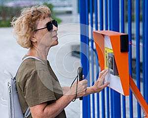 An elderly blind woman reading a text in braille. Button for calling help for people with disabilities.