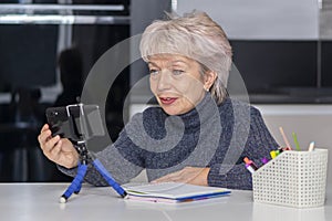 An elderly blonde woman in her 60s and 65s communicating via video link. Concept: remote work, communicating with loved ones via t