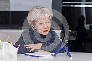 An elderly blonde woman in her 60s and 65s makes a video call, smiling happily.