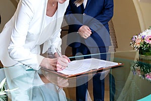 Elderly bride and groom signing marriage agreement at desk. Woman& x27;s hand holding pen and signing paper document