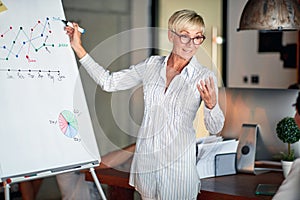 An elderly business woman carefully listen to her female colleague explaining a graph on the panel to her at workplace. Business,