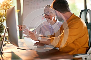 An elderly business woman and her young male colleague are talking about a computer screen content while they working at the desk