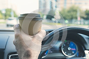Elderly Businessman drinking coffee from paper cup while driving a car on the highway. Selective focus.