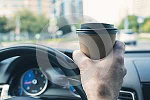 Elderly Businessman drinking coffee from paper cup while driving a car on the highway. Selective focus.