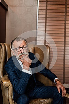 Elderly businessman in formal suit with whiskey and cigar at lux
