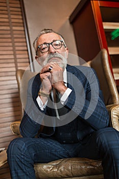 Elderly businessman in formal suit with whiskey and cigar at luxury interior