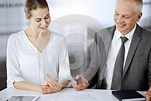 Elderly businessman and woman sitting and communicating in sunny office. Adult business people or lawyers working
