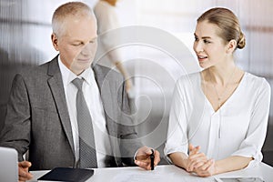 Elderly businessman and woman sitting and communicating in sunny office. Adult business people or lawyers working