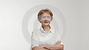 An elderly businesswoman or entrepreneur with a direct gaze and ironic smile on face crosses arms over chest