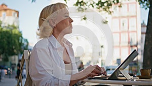 Elderly businesswoman typing laptop at sunny street cafe closeup. Serious senior