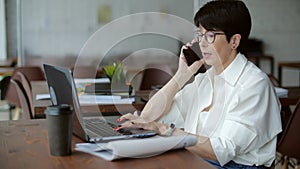 Elderly businesswoman working in modern office, making phone call to potential client, having nice conversation