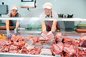 Elderly butcher shop seller laying out raw pork ribs in display case