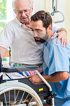 Elderly care nurse helping senior from bed to wheel chair