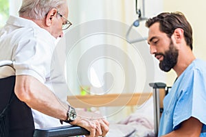 Elderly care nurse helping senior from bed to wheel chair