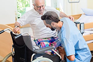 Elderly care nurse helping senior from wheel chair to bed