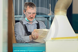 An elderly carpenter of Caucasian appearance works in a carpentry workshop. Processing of boards on a lathe.