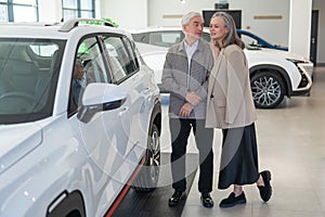 An elderly Caucasian couple chooses a new car at a car dealership.