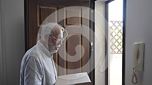 Elderly Caucasian male pensioner on the door of his house receives a postal package from the courier.