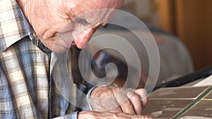 An elderly Caucasian man over 70 years old looks at a photo album while sitting at a table at home. Good memories of youth. pensio