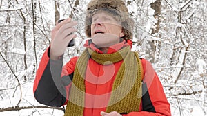 Elderly Caucasian man walks through the winter forest, trying to catch a signal on a smartphone. Thick dense thicket of