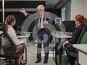 Elderly Caucasian man wearing a clown nose swears at his subordinates.